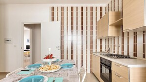 A modern kitchen with a dining area, featuring a stove, oven, and a table set for a meal. - Residence Kalura - Trilo con Balcone (SP) (Porto Cesareo)