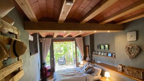 A bedroom with a wooden ceiling, a bed with pillows, a nightstand with a lamp, and a view of the outdoors through a window. - Beautiful studio/apartment with air conditioning and use of pool.  (Begur)