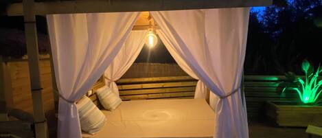 A wooden deck with a canopy bed, string lights, and a green plant.