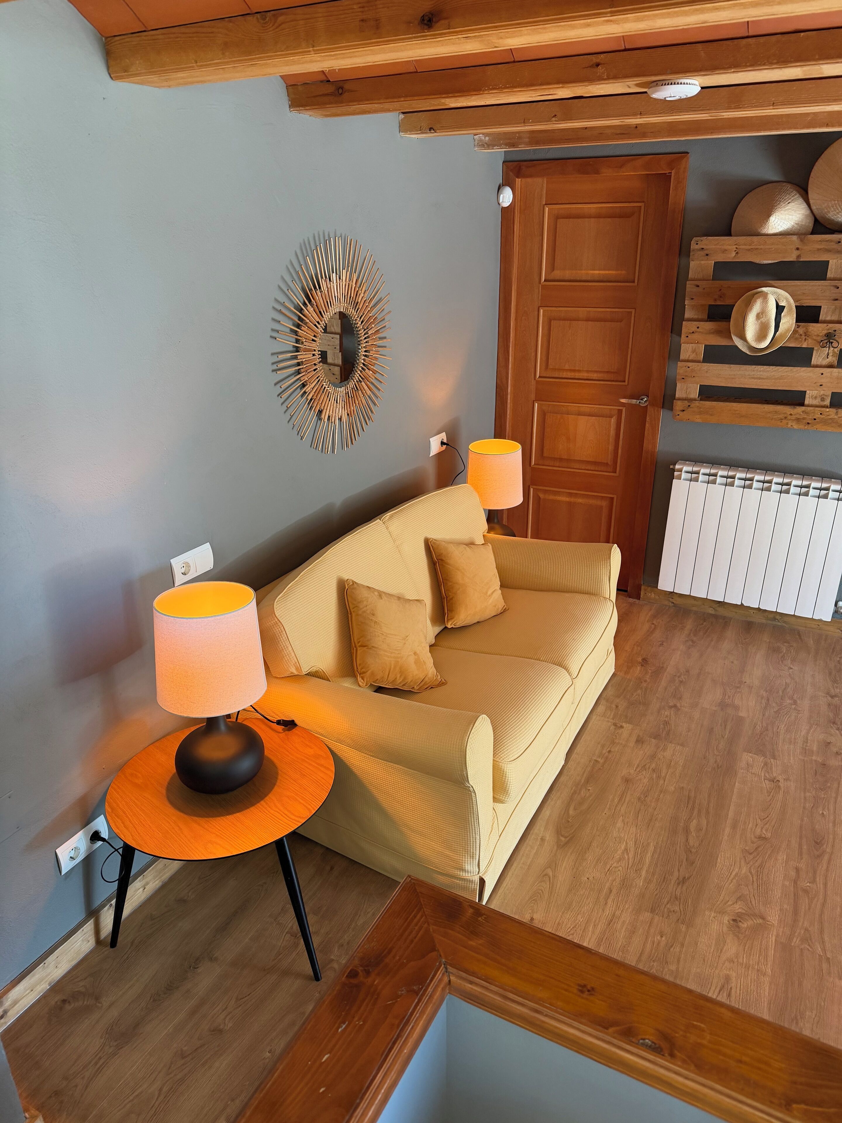 A cozy room with a beige sofa, two lamps, a wooden wall decor, and a door.