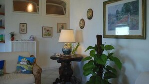 A living room with a sofa, a table with a lamp, a potted plant, and framed pictures on the wall.