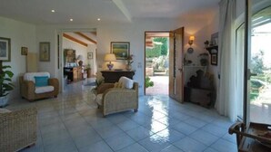 A spacious living room with a tiled floor, wicker furniture, and a view of the outdoors through a large window.