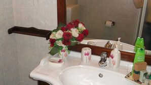 Ein Badezimmer mit weißem Waschbecken, einem Spiegel, einem hölzernen Handtuchhalter, einem Blumenstrauß und Toilettenartikeln.