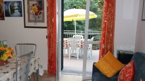 Ein Wohnzimmer mit einer Couch, einem Esstisch mit Stühlen und Blick auf eine Terrasse mit einem gelben Sonnenschirm.