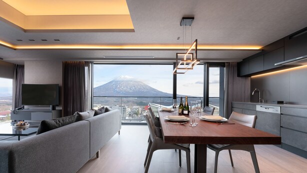 A modern dining area with a wooden table and chairs, a sofa, and a television on a stand. - Sansui Niseko (Kutchan)