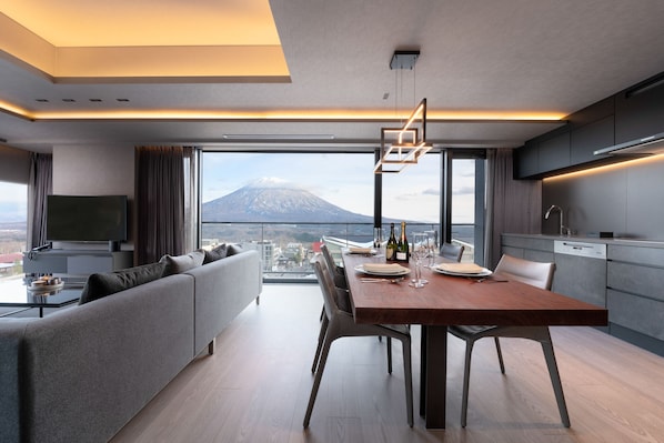 A modern dining area with a wooden table and chairs, a sofa, and a television on a stand. - Sansui Niseko (Kutchan)