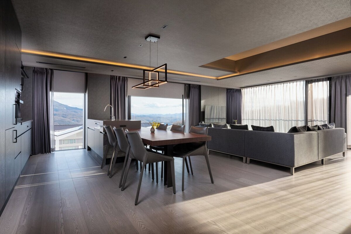 A modern hotel room with a dining area, a sofa, and a view of the mountains.