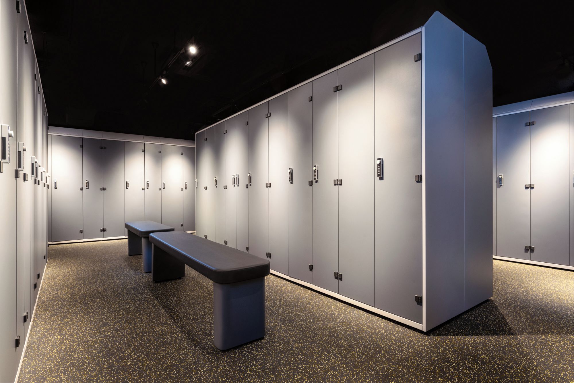 A row of lockers with a bench in the center, a ceiling light, and a speckled floor.