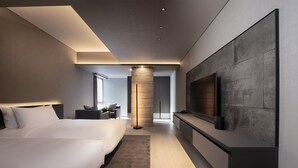 A modern hotel room with a large bed, a seating area, a TV mounted on the wall, and a central pillar. - Sansui Niseko (Kutchan)