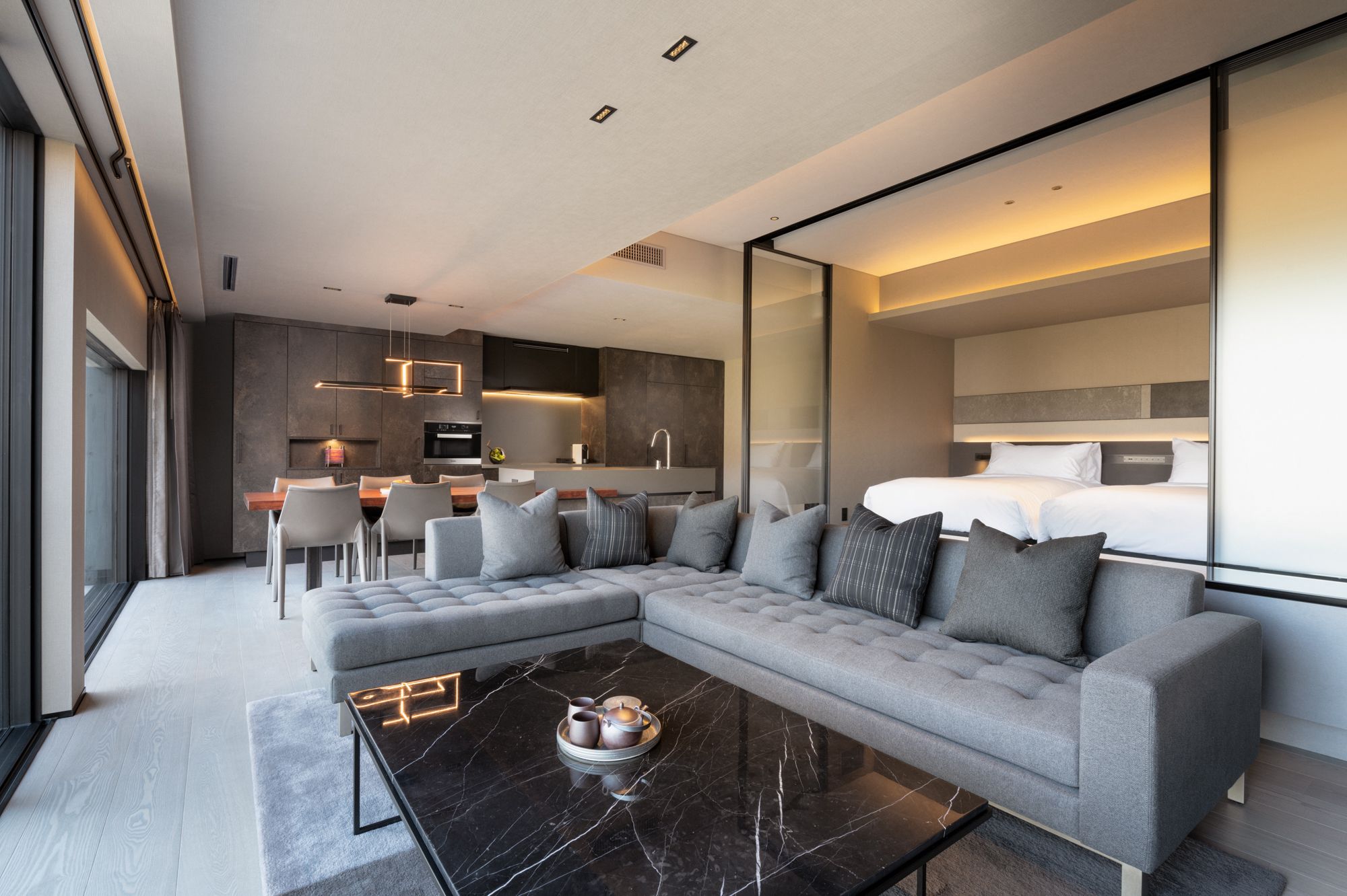 A modern hotel room with a sectional sofa, a dining area, and a kitchen.