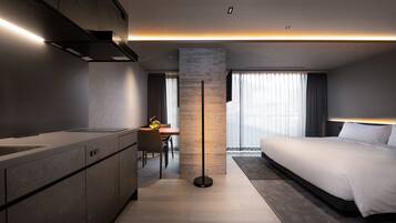 A modern hotel room with a kitchenette, a dining area, and a large bed.