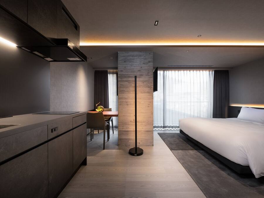 A modern hotel room with a kitchenette, a dining area, and a large bed.