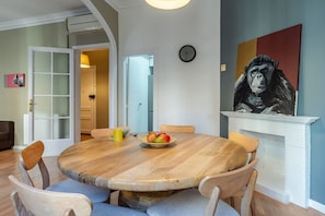 A dining area with a round wooden table, chairs, a clock, and a painting on the wall.