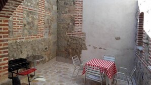 Un patio con paredes de piedra, una mesa y sillas, una parrilla negra pequeña y una pared blanca.