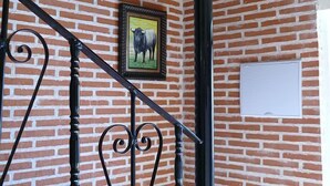 Una pared de ladrillo con un cuadro enmarcado de un toro, una escalera de metal negro y una pizarra en blanco.
