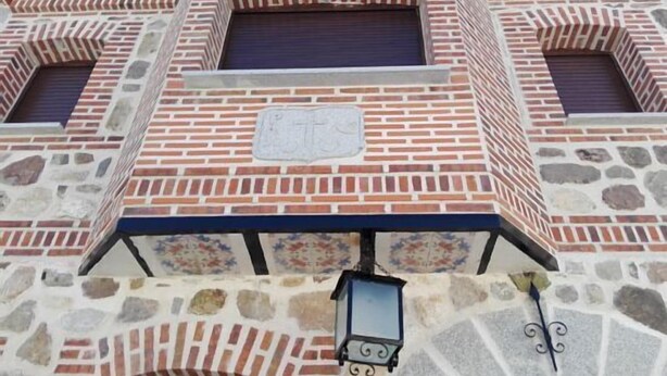 Un edificio con fachada de piedra y detalles en ladrillo rojo, así como un farol decorativo.