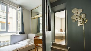 Une chambre à coucher de taille réduite, dotée d’un lit escamotable, d’un petit bureau et d’un grand miroir.