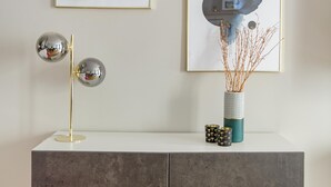Un intérieur moderne avec un meuble gris, un lampadaire et deux œuvres d’art encadrées accrochées au mur.