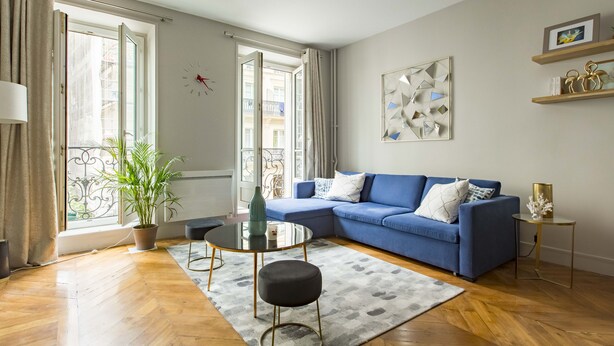Un salon moderne avec un canapé bleu, une table basse en verre, une plante en pot et une vue sur le balcon extérieur.