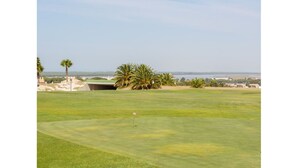 Ein Golfplatz mit freiem Blick auf das Meer und einer entfernten Skyline.