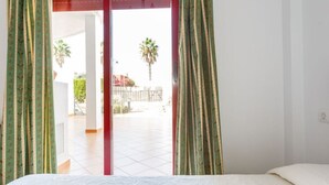 Ein Schlafzimmer mit Bett, Blick auf einen Balkon mit Fliesenboden und einer roten Tür.