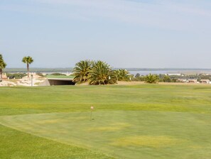 A golf course with a clear view of the ocean and a distant city skyline.