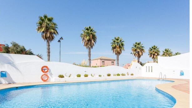 Ein Pool mit gewölbter Kante, umgeben von einer weißen Mauer und Palmen.