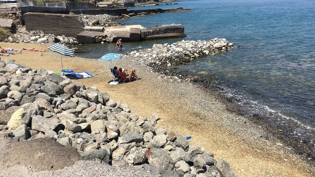 A rocky beach with clear water, a few umbrellas, and a distant view of hills and buildings. - CASA PARADISO Vacanze  (Costa Saracena - Castelluccio)