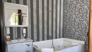A bathroom with a bathtub, a vanity with a mirror, and striped wallpaper. - Suite with private jacuzzi in the room (Arenas)
