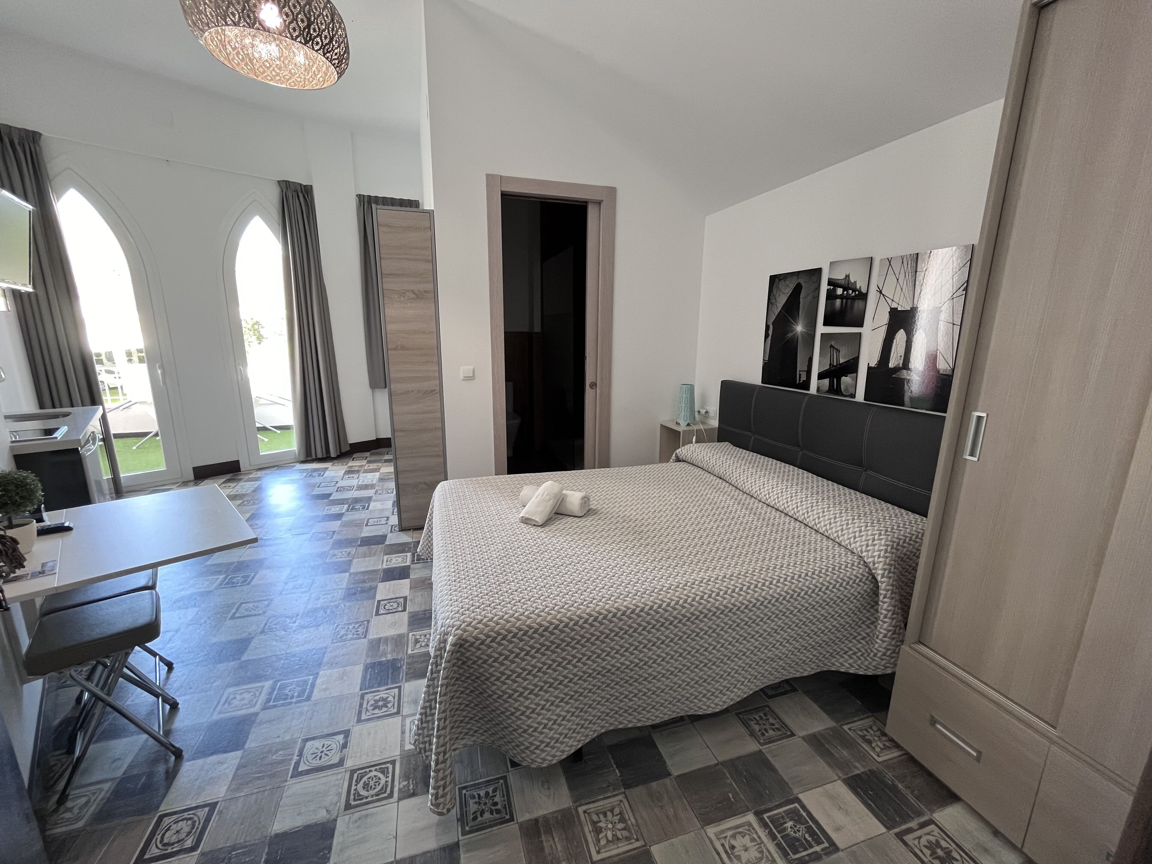 A hotel room with a bed, a desk, and a chair. There is a door leading to a balcony.