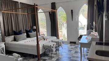 A bedroom with a four-poster bed, a desk, and a view of the outdoors.