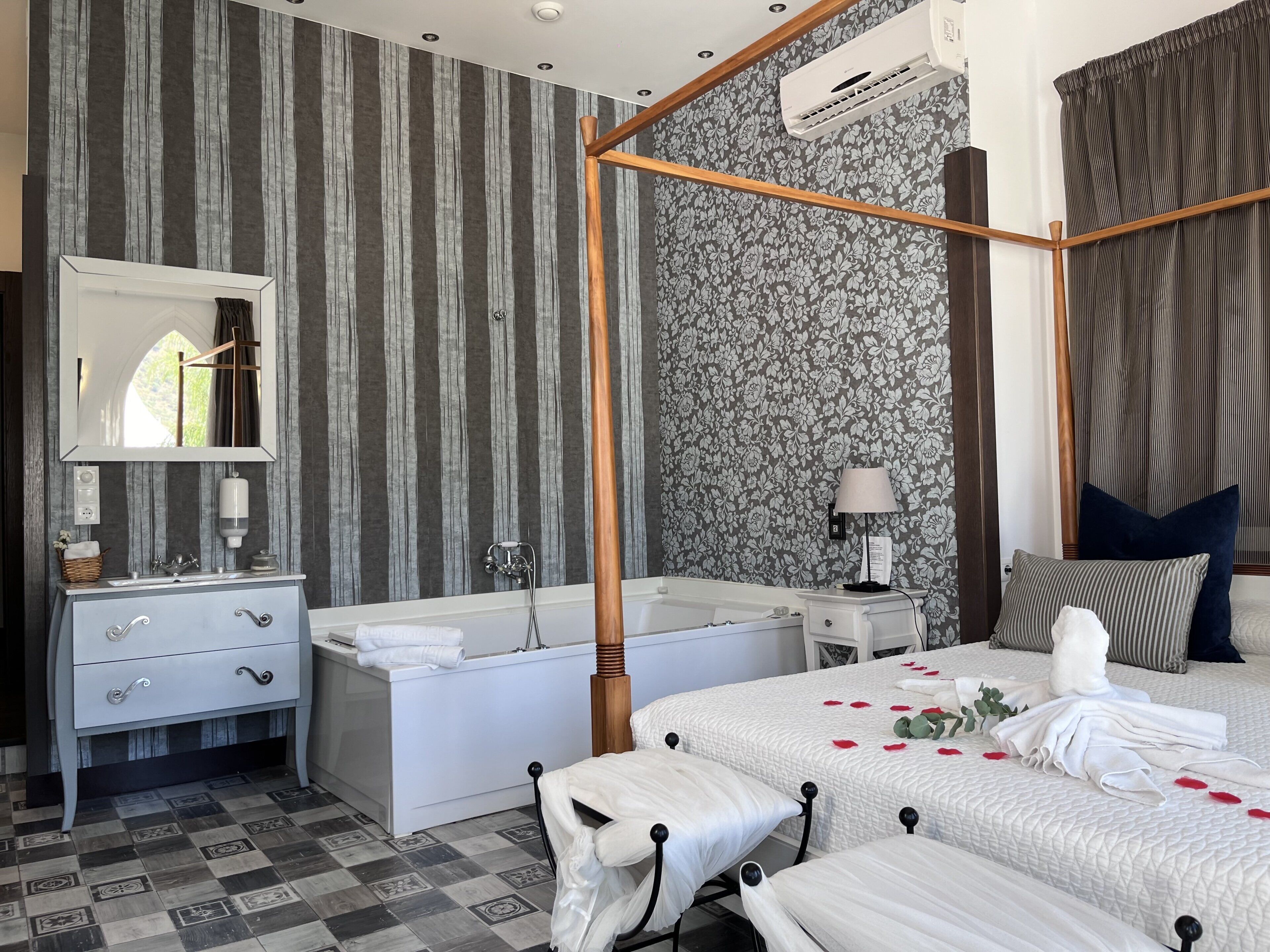 Une chambre à coucher avec un lit à baldaquin, une salle de bain séparée avec une baignoire, un meuble-lavabo avec un miroir et un climatiseur fixé au plafond.