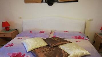 Ein Schlafzimmer mit einem Bett, floralem Bettzeug, einem Nachttisch mit Lampe und einem Wandventilator.