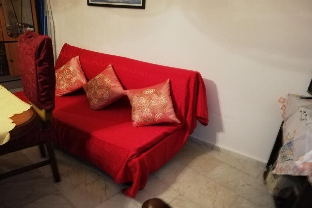 Een rode bank met patroon kussens in een kamer met een betegelde vloer en een ingelijst kunstwerk aan de muur.
