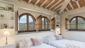 A bedroom with two beds, wooden arched windows, white shelving, and a view of a mountainous landscape. - Torre La Ripa 8, Emma Villas (Cortona)