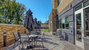 An outdoor patio area with tables and chairs, a stone wall, and a building with large windows. - Fairfield Inn & Suites by Marriott Appleton (Appleton)