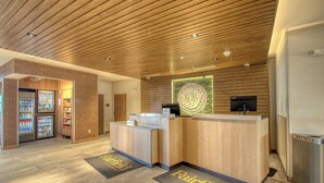 A hotel reception area with a wooden ceiling, a reception desk, a digital screen, a refrigerator, and a recycling bin. - Fairfield Inn & Suites by Marriott Appleton (Appleton)