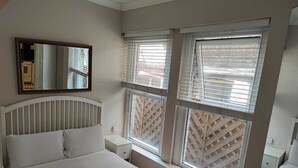 Ein Schlafzimmer mit Bett, Nachttisch, Spiegel und Fenstern mit Jalousien.
