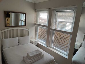 A bedroom with a bed, a nightstand, a mirror, and windows with blinds.