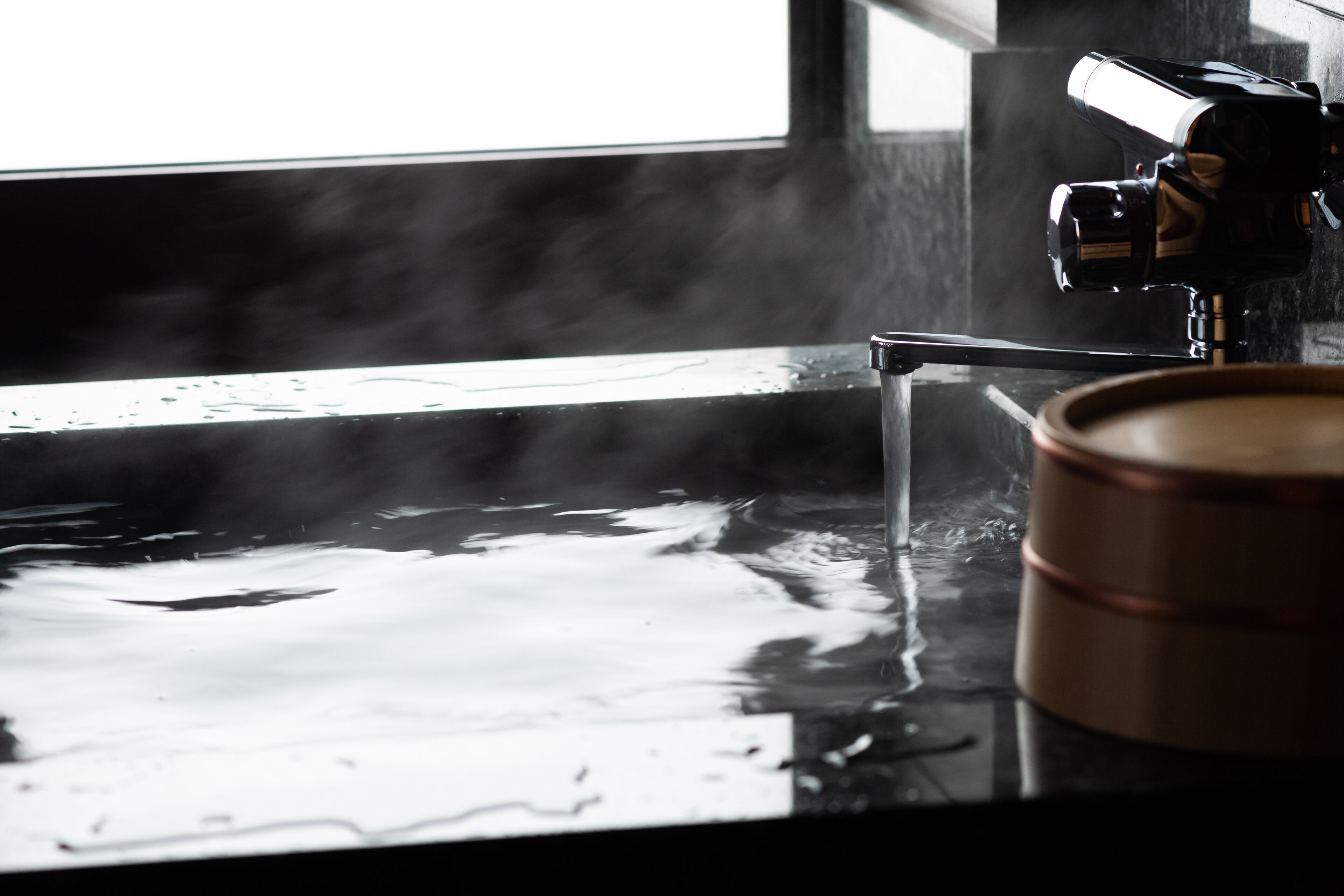 Une douche à vapeur dotée d’une paroi en verre transparent, d’un seau en bois et d’un appareil photo fixé sur un trépied.