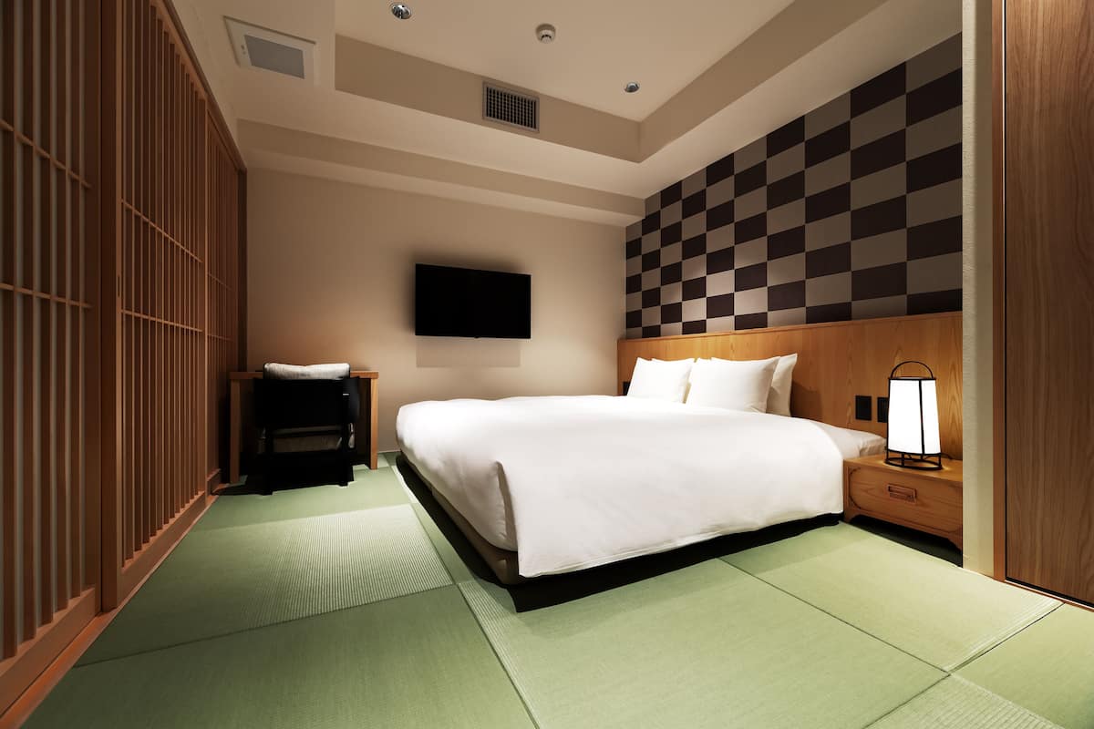 A hotel room with a large bed, a bedside table with a lamp, a TV mounted on the wall, and a checkered wall design.