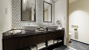 A modern bathroom with two large sinks, a vanity with a mirror, and a towel rack with neatly folded towels.