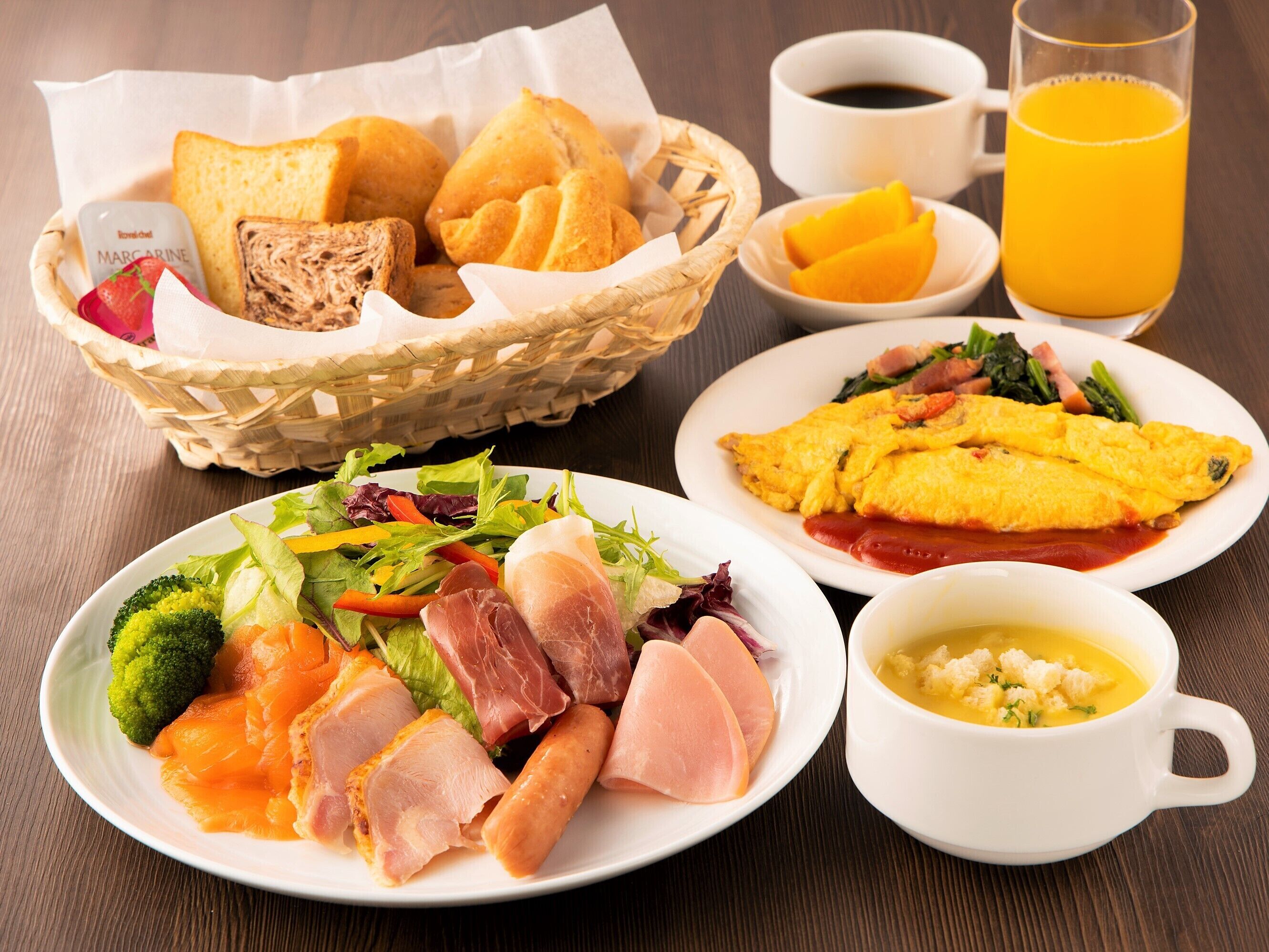 Mesa de café da manhã com torradas, pães, salada, presunto, ovos e uma tigela de sopa.