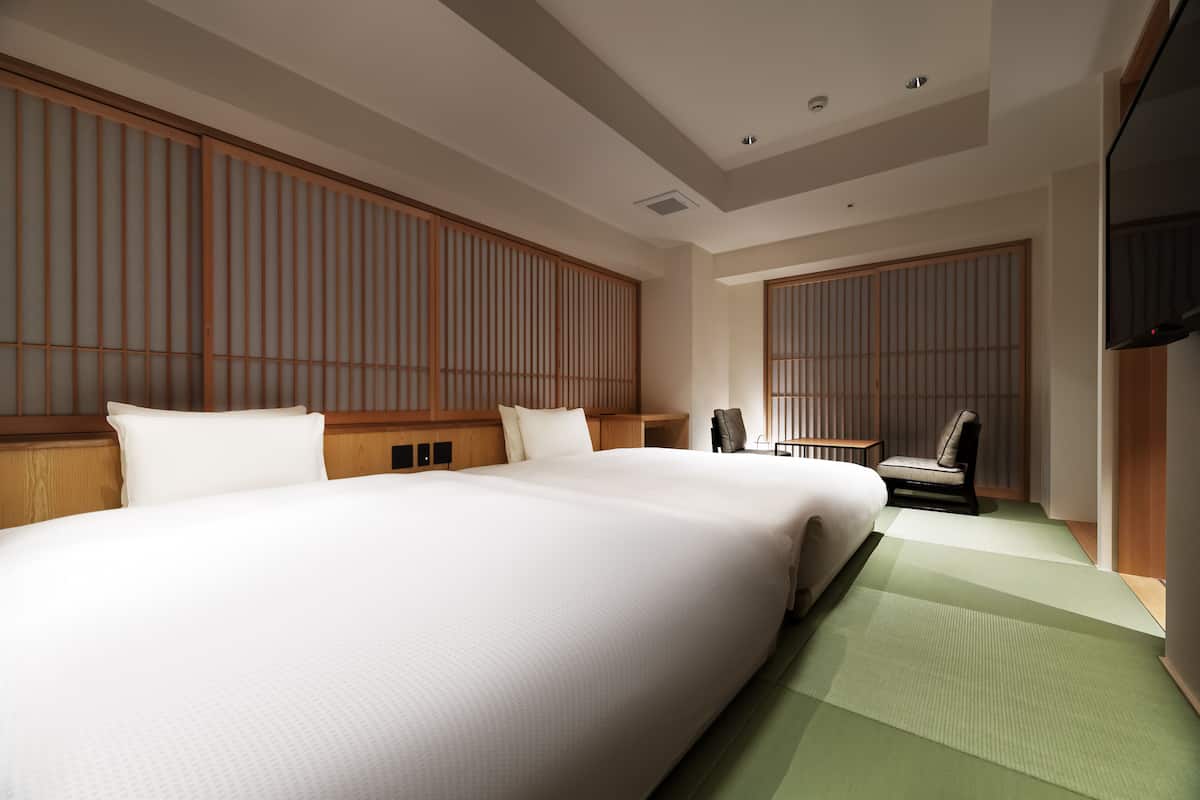 A hotel room with a large bed, a chair, a small table, and sliding doors.