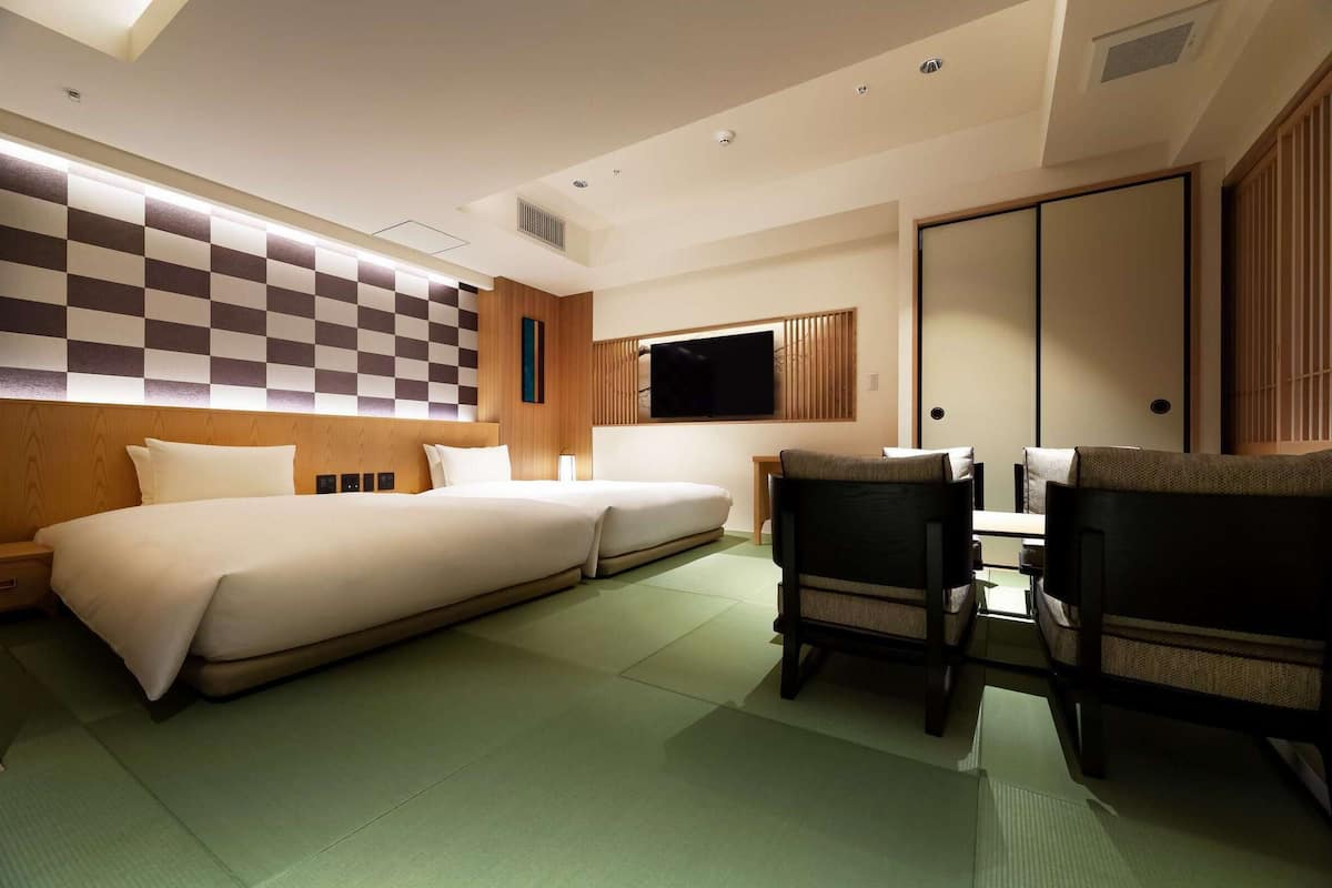 A hotel room with a large bed, a TV, a wooden headboard, and a traditional sliding door.