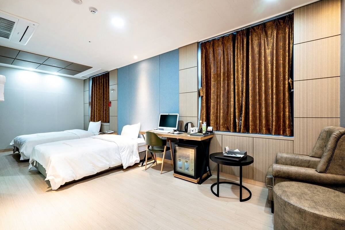 Habitación de hotel con dos camas, un escritorio con computadora, una mesita y una silla.