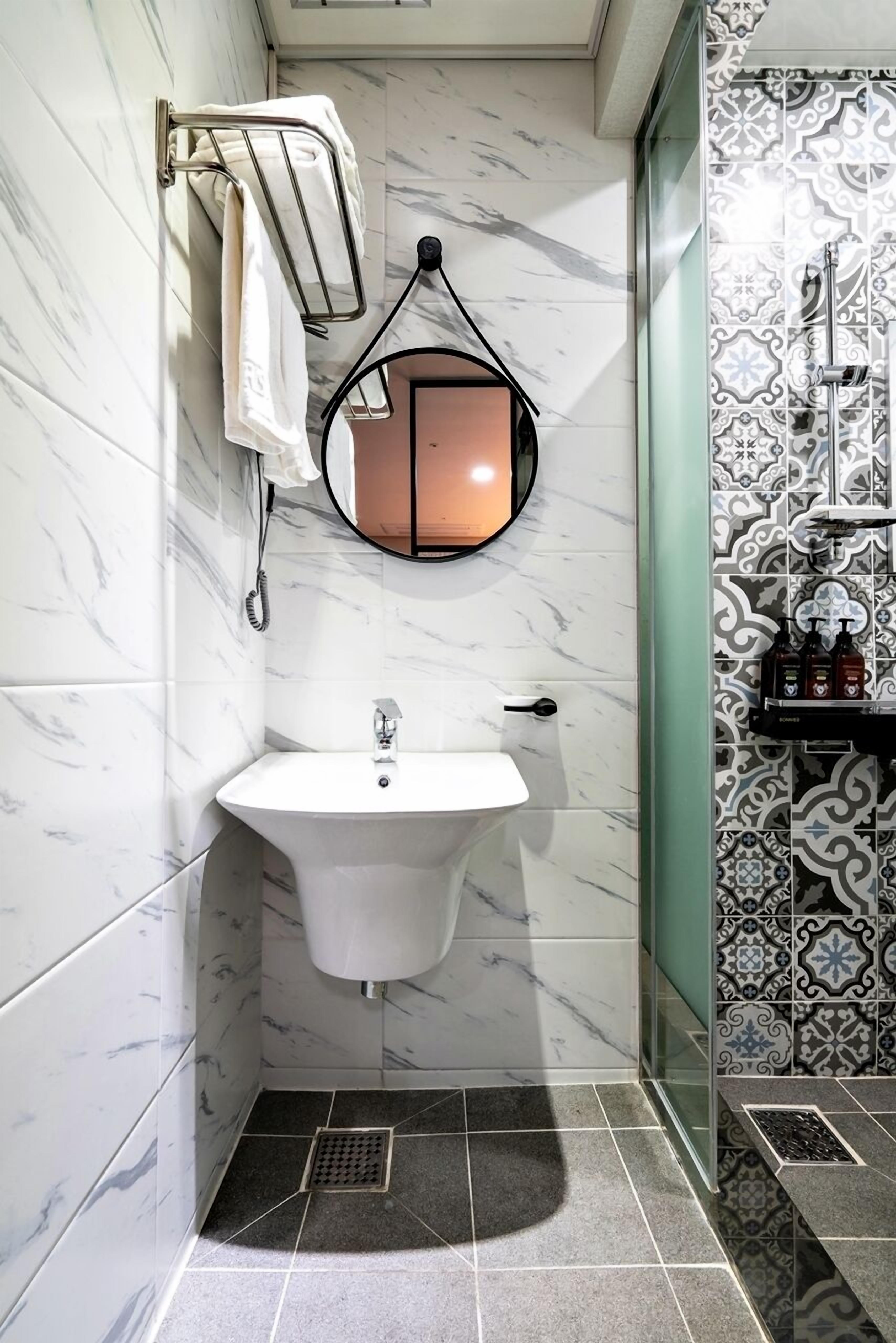 Un bagno con un lavandino bianco, un porta asciugamani, uno specchio e piastrelle decorate.