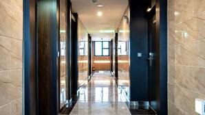 En modern hotellkorridor med reflekterande golv, mörka trädörrar och en central ljuskälla.