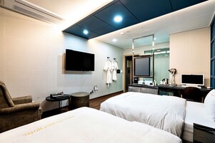 A hotel room with two beds, a TV, a mirror, and a desk with a computer.