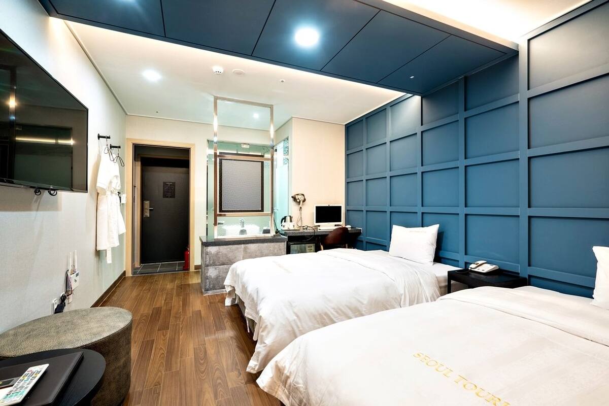 Habitación de hotel con dos camas, un escritorio con ordenador, un espejo y un televisor montado en la pared.
